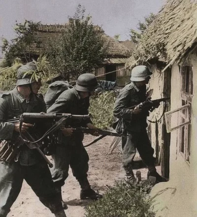 wojna - Niemieccy żołnierze, uzbrojeni w MP40, przeszukują wioskę Gatnoje w poszukiwa...