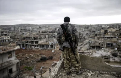 Talvisota - Musa, 25-letni kurdyjski bojownik spogląda na ruiny syryjskiego miasta Ko...