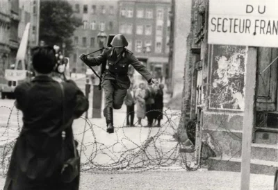 flager - NRD-owski żołnierz Conrad Schumann dezerteruje i przeskakuje przez drut kolc...