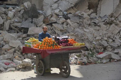 Antiax - Syryjski sprzedawca owoców czeka na klientów na tle zniszczonego budynku. Al...
