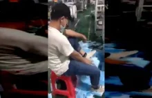 Pracownik wyciera sobie buty nowo wyprodukowanymi maseczkami
