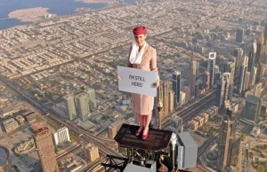 Stewardesa na najwyższym budynku świata, a za nią przelatuje samolot