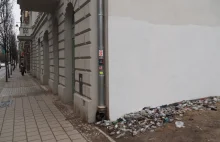 Łódź. Robotnicy pomalowali ścianę kamienicy, omijając stos butelek po wódce