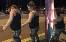 Pijana kobieta atakuje plakat na przystanku autobusowym.