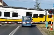 Bus osobowy stoi między szlabanem a przejeżdżającym pociągiem.